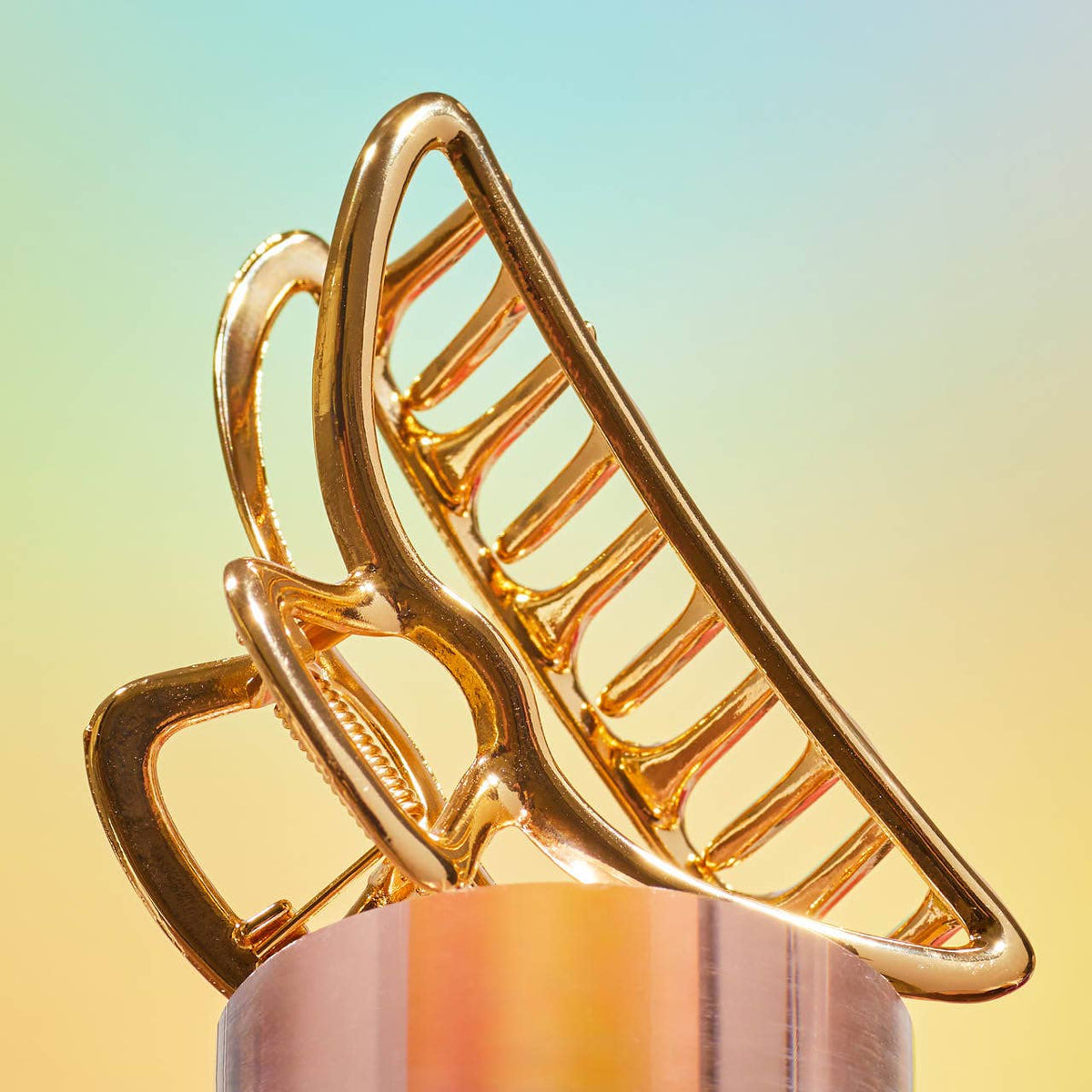 Close-up of a shiny gold claw clip on a soft pastel background