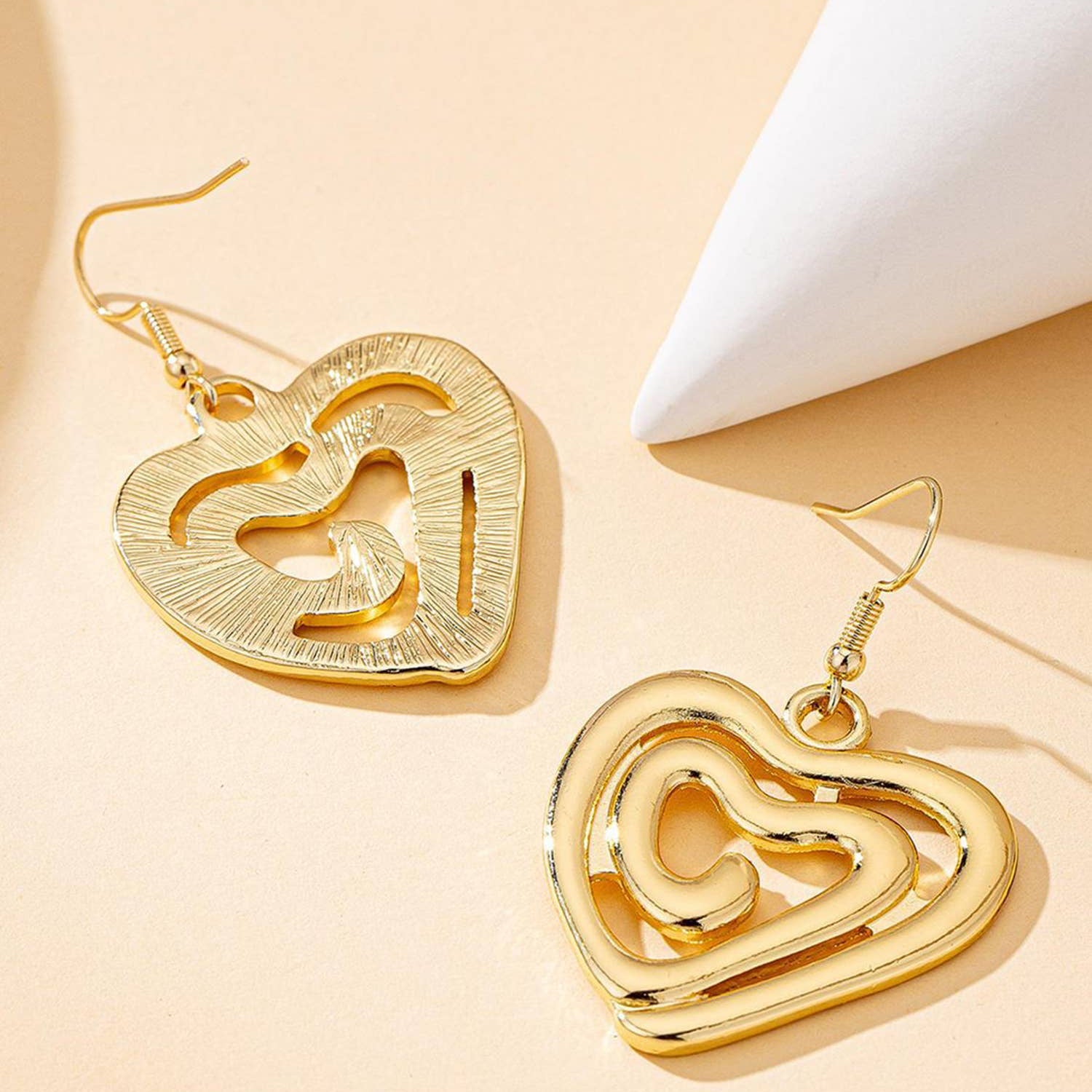 Gold heart-shaped earrings on a beige background
