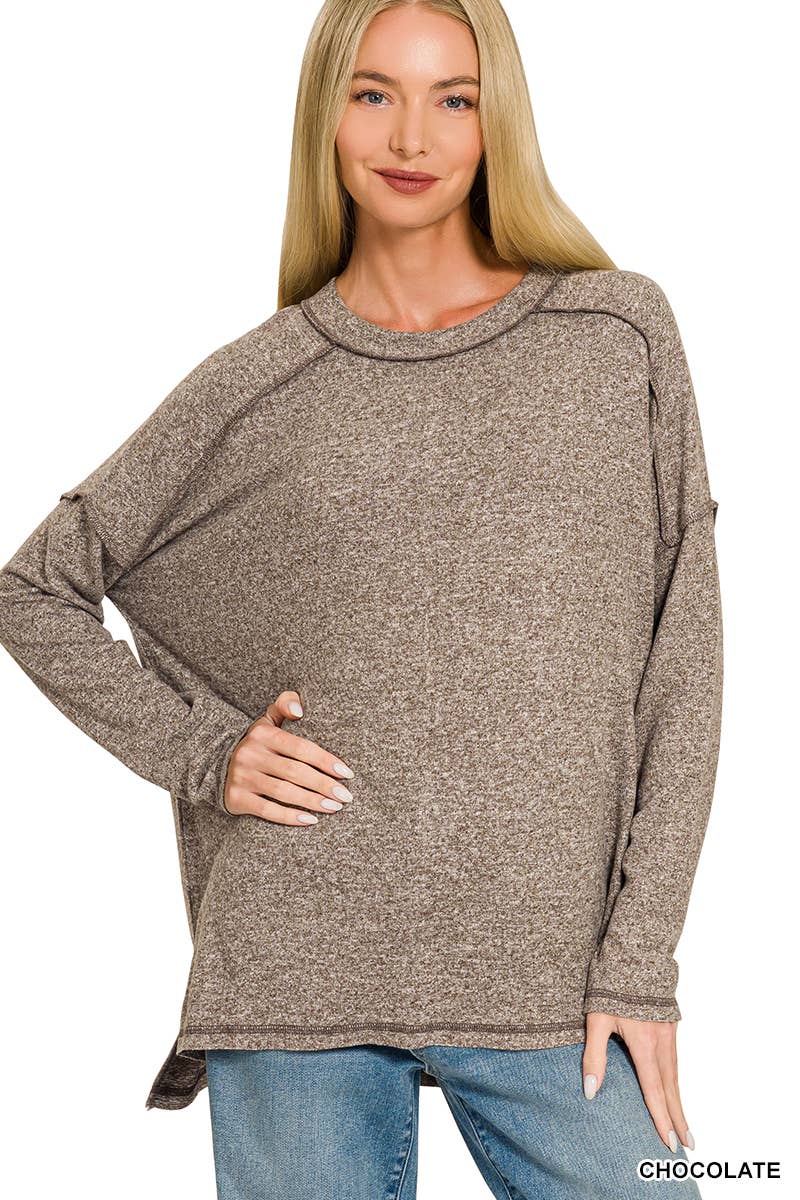 Woman wearing an oversized chocolate brown melange hacci knit top with exposed seams, long sleeves and a hi-low hem, paired with jeans
