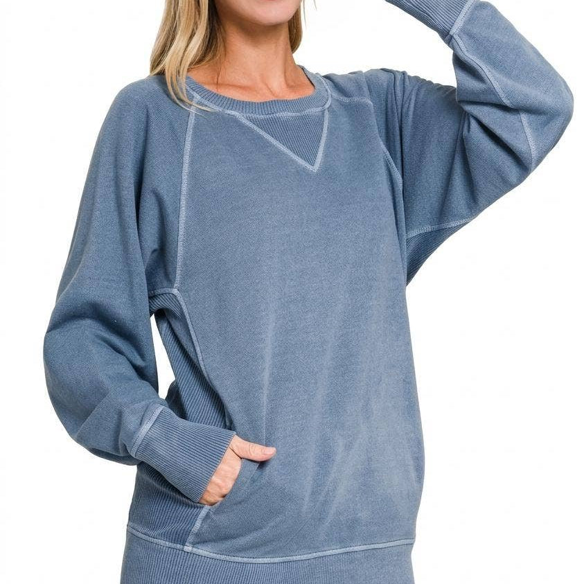 Woman wearing a washed dusty blue French terry pullover with raglan sleeves, V-stitch neckline, contrast stitching and front pockets, styled with dark jeans