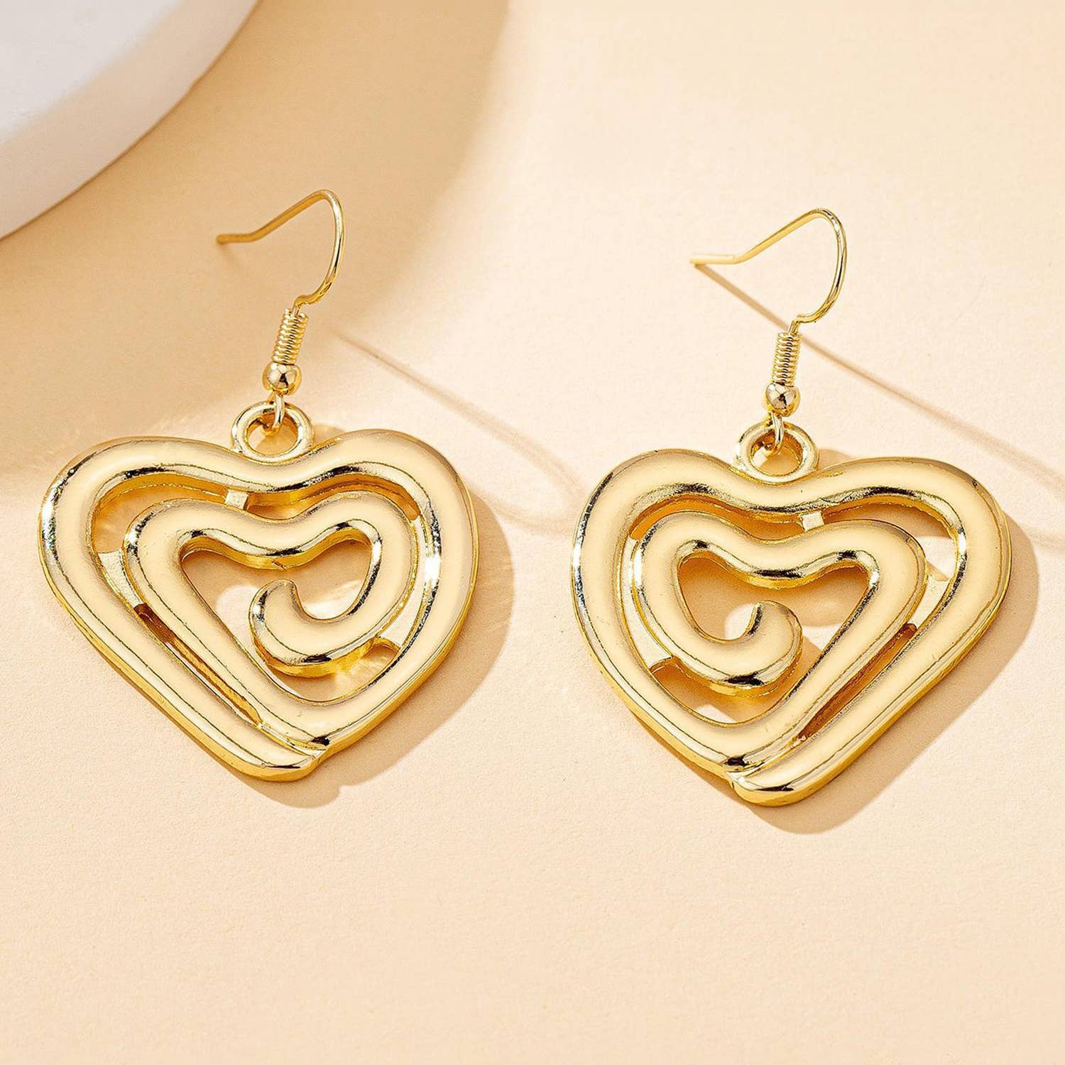 Gold heart-shaped earrings on a beige background