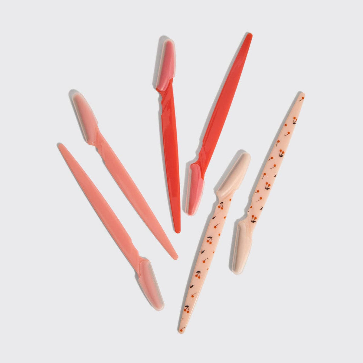 Six KITSCH dermaplaning tools in cherry print, peach, pink and red laid out on white