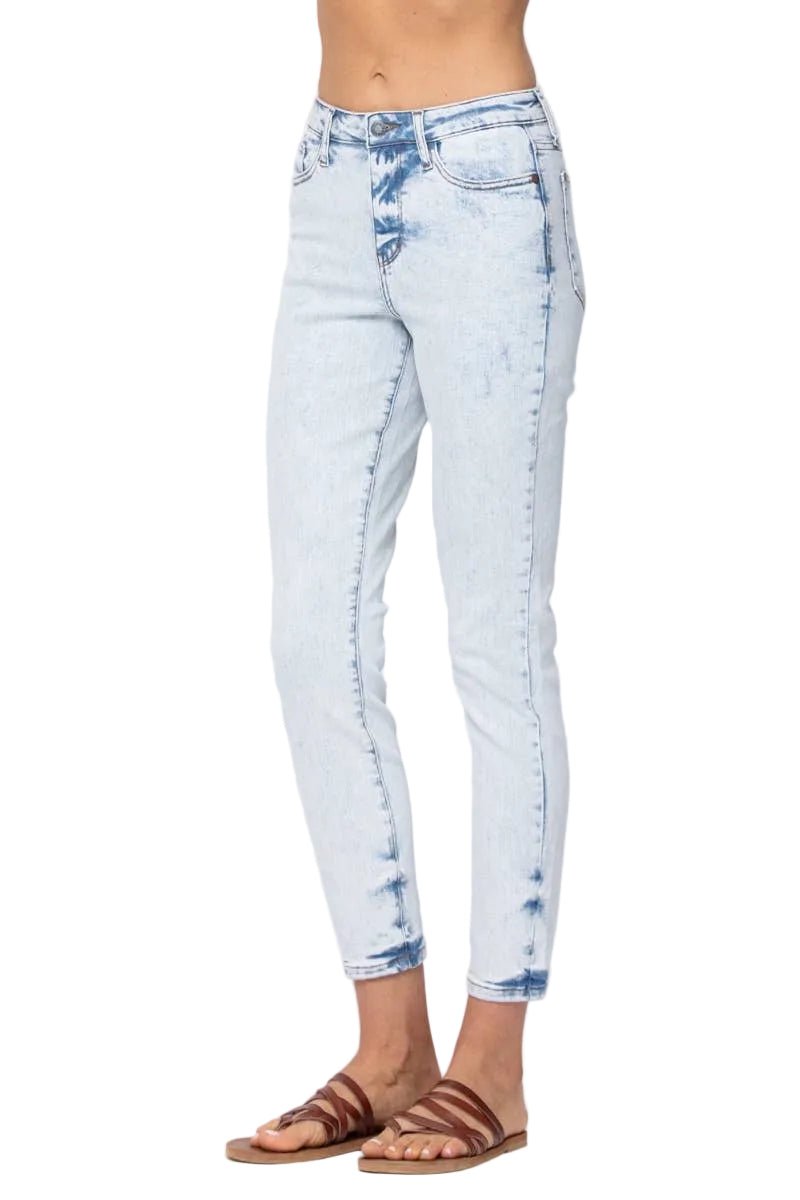 A person wearing light-wash blue acid-wash cropped jeans with brown slide sandals, shown from the waist down against a plain white studio background.