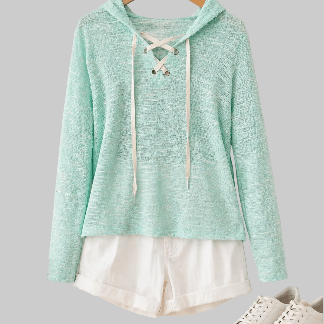 Mint green hoodie with lace-up front on a hanger, white shorts, and white sneakers on a light wooden floor.