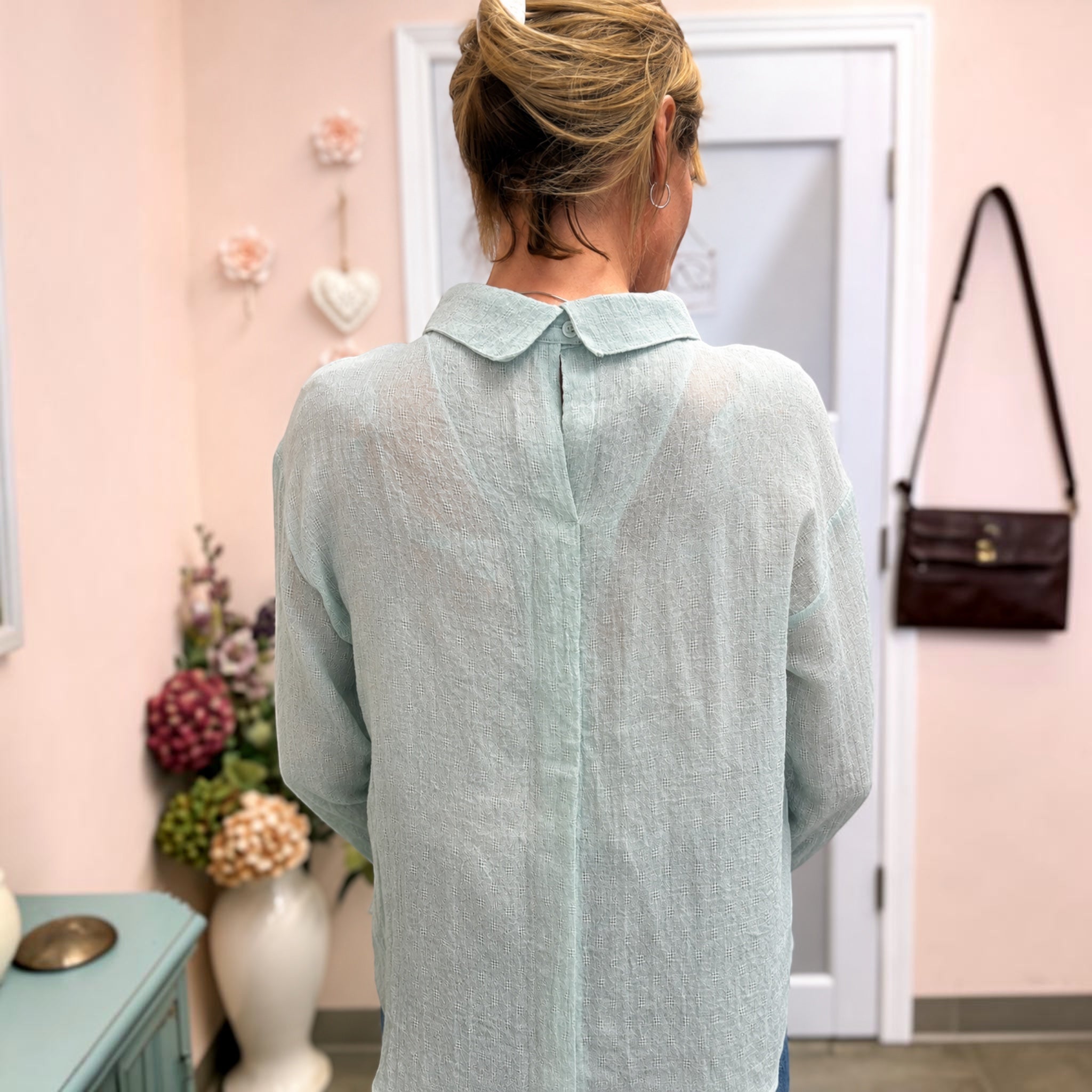 backside of a mint line top on a woman. with pink walls.