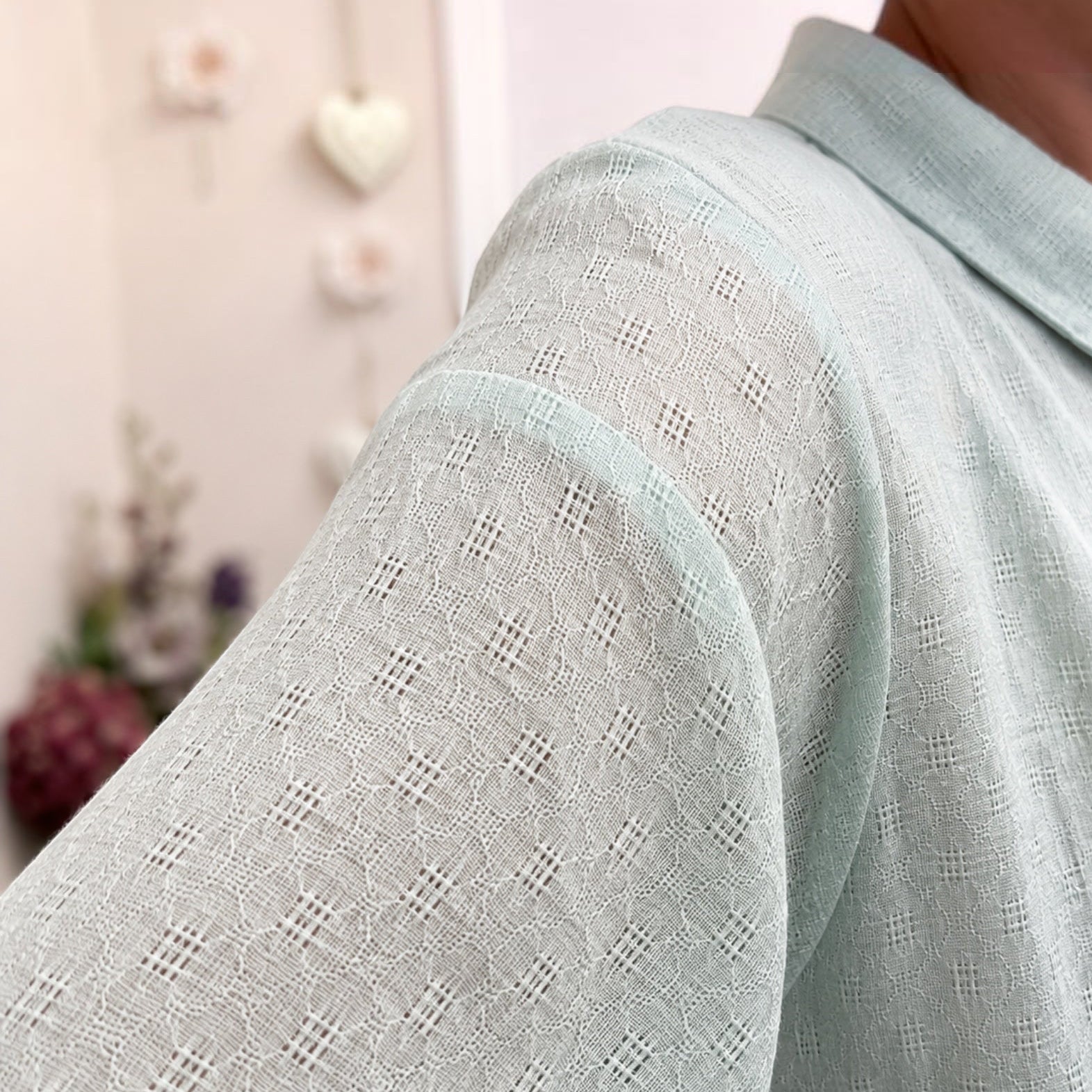 Close-up of a person wearing a pale mint green long-sleeve shirt with a textured eyelet pattern, showing the collar and shoulder area.