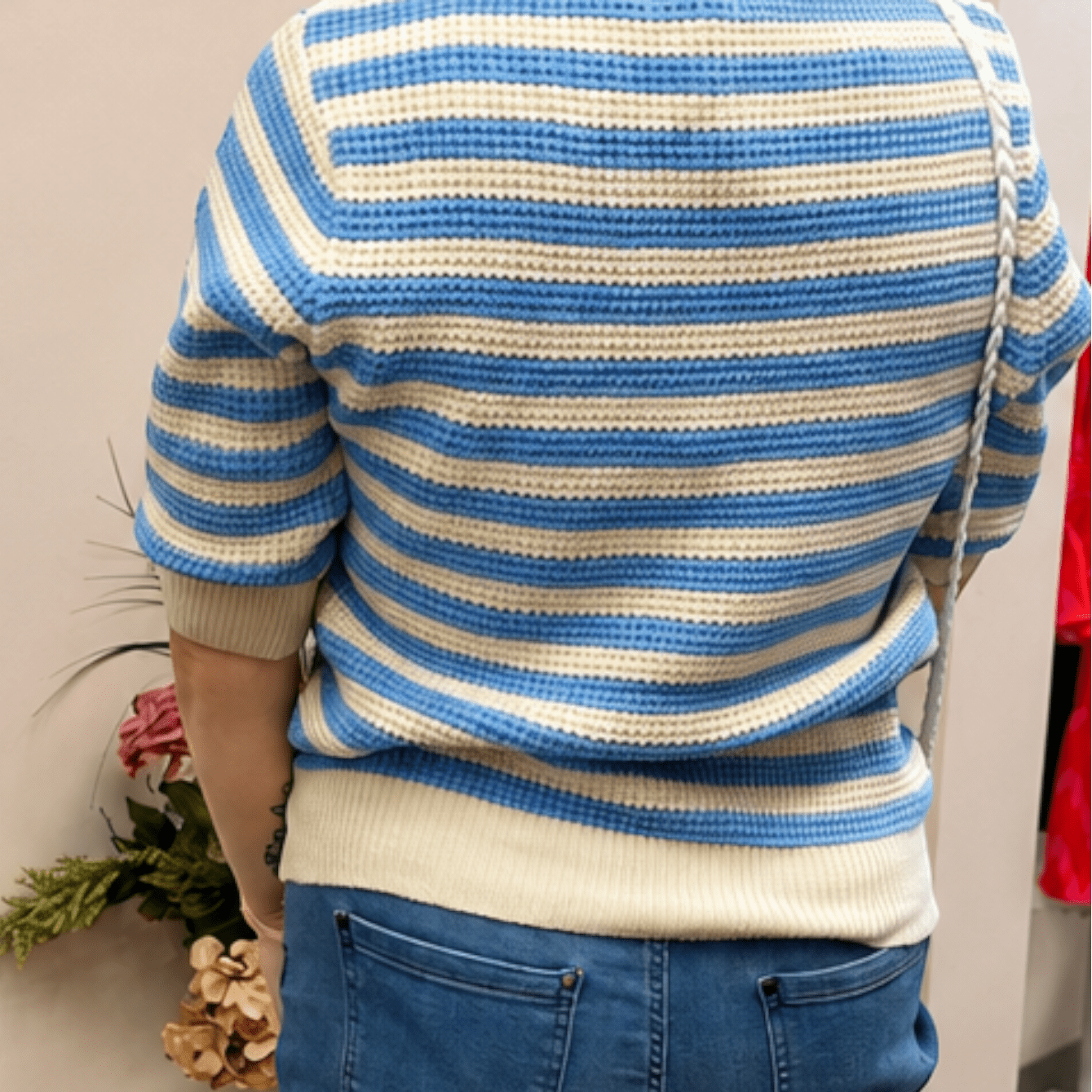 Person wearing a blue and white striped sweater and blue shorts, standing in a room with a neutral wall.
