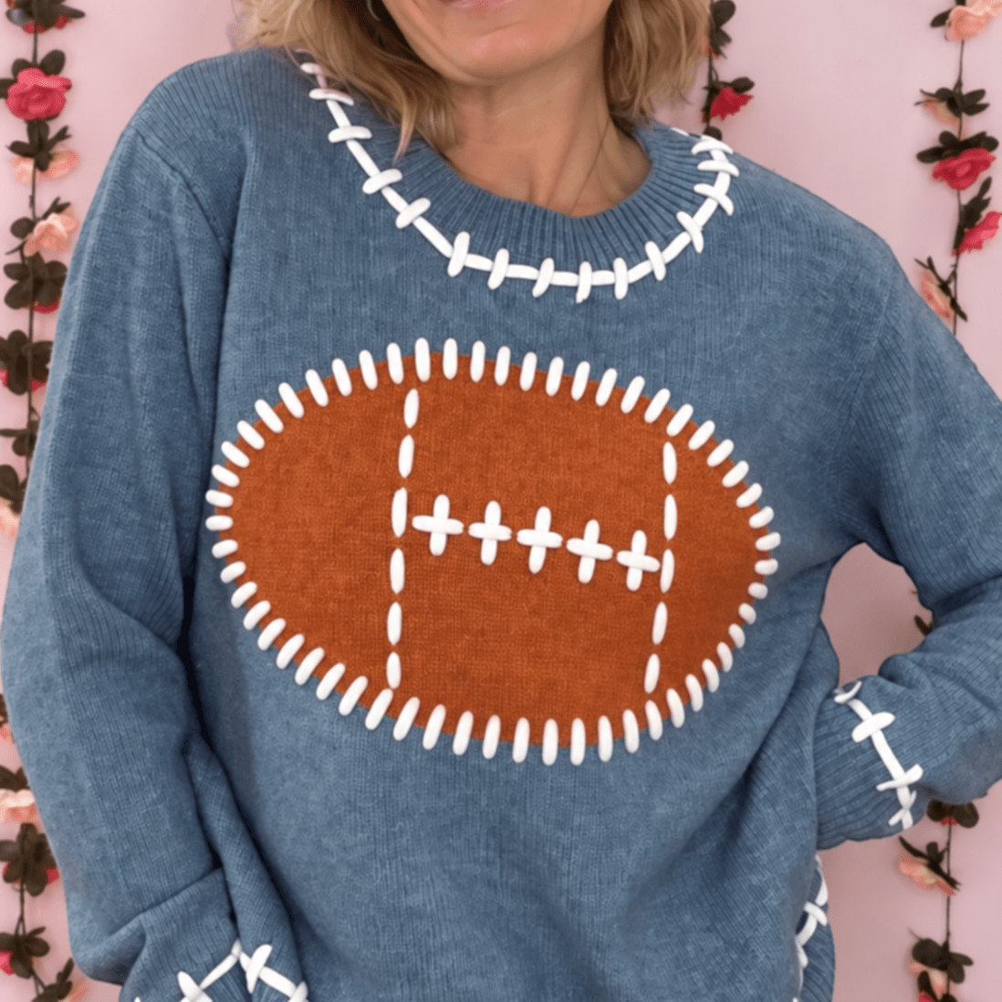 Woman wearing a dusty blue football knit sweater with a brown football graphic and white stitch details