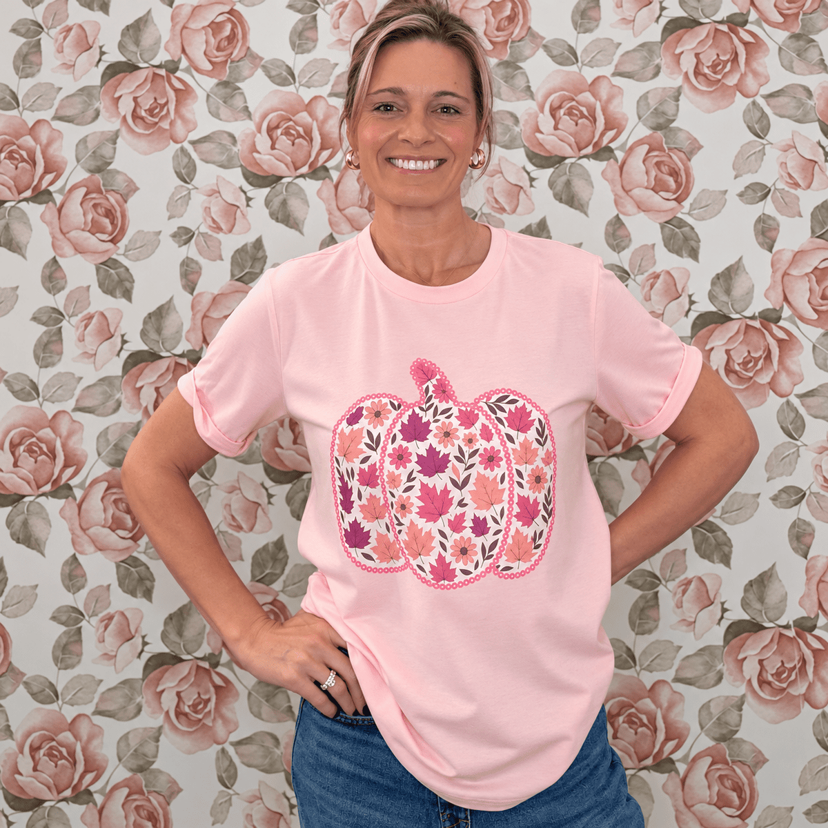 Woman wearing a pink short sleeve tee with a floral pumpkin graphic, paired with medium wash jeans