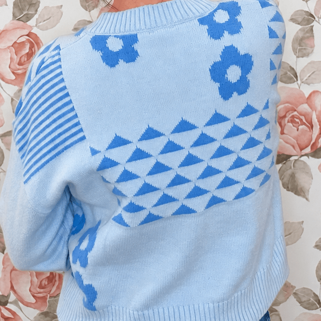 Close-up of light blue knit sweater back showing blue daisy, stripe and geometric triangle knit details