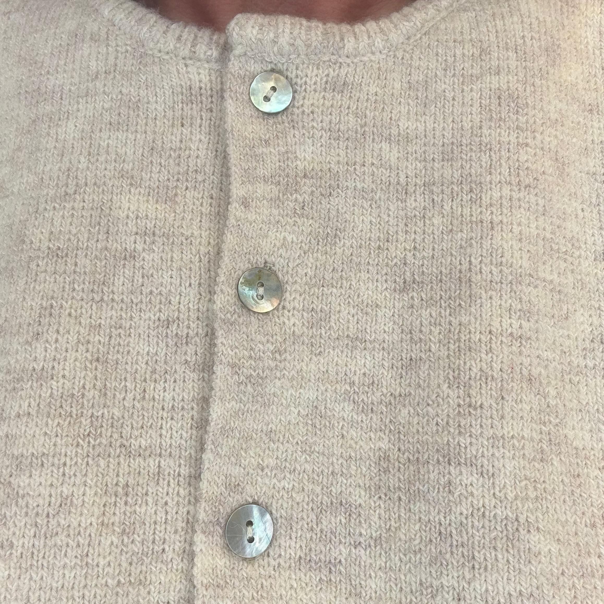 Close-up of a beige-colored knit cardigan sweater with three mother-of-pearl buttons, worn by a model.