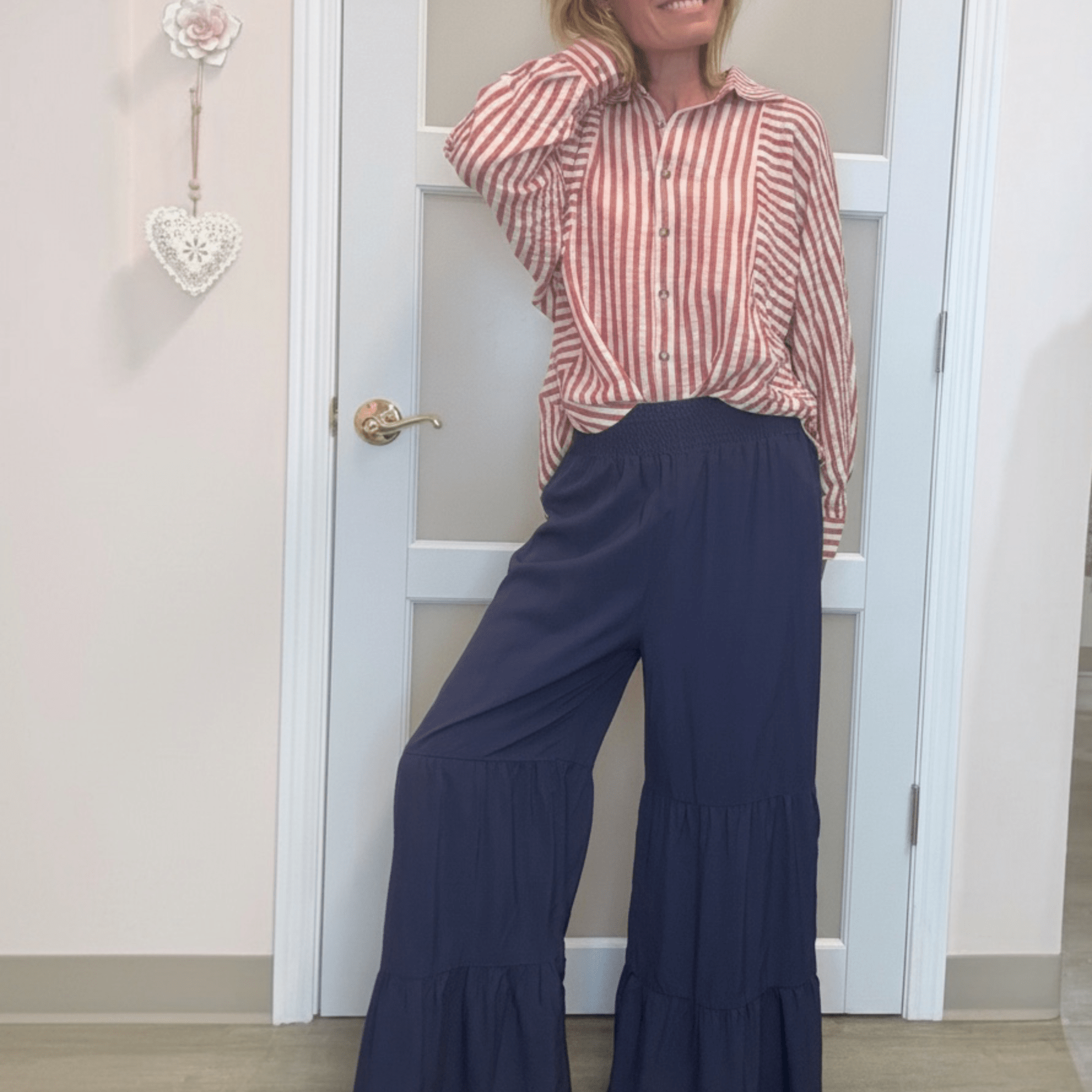 woman in red and white striped shirt with blue ruffle pants. standing against a white door