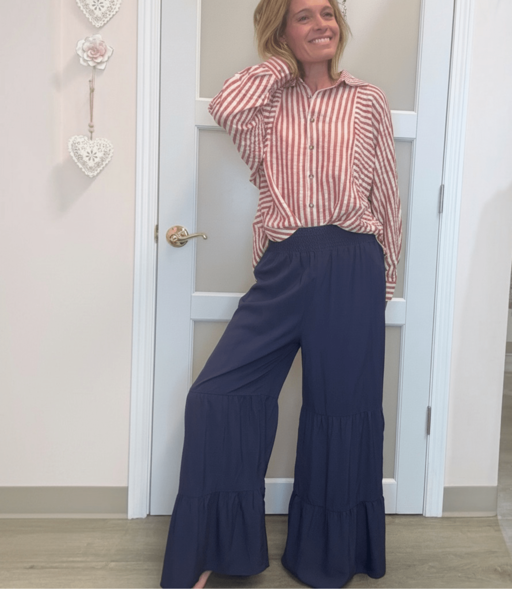 woman in red and white striped shirt with blue ruffle pants. standing against a white door
