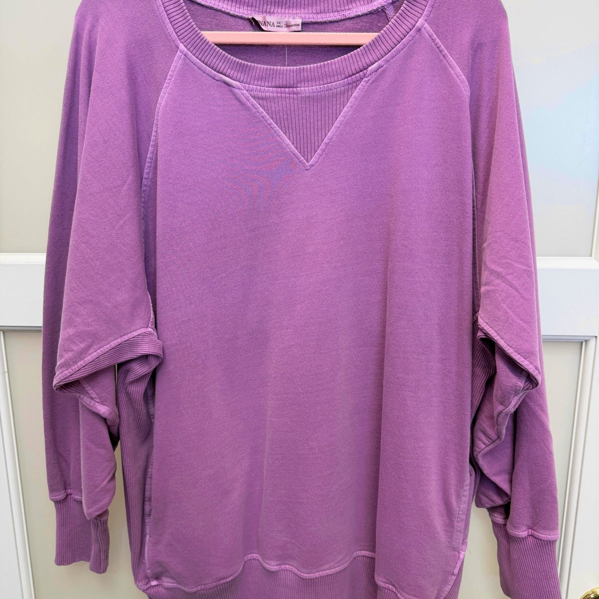 Flat lay of the plus size crewneck sweatshirt on a hanger showing the raglan sleeves, V-stitch detail at the neckline and ribbed cuffs and hem