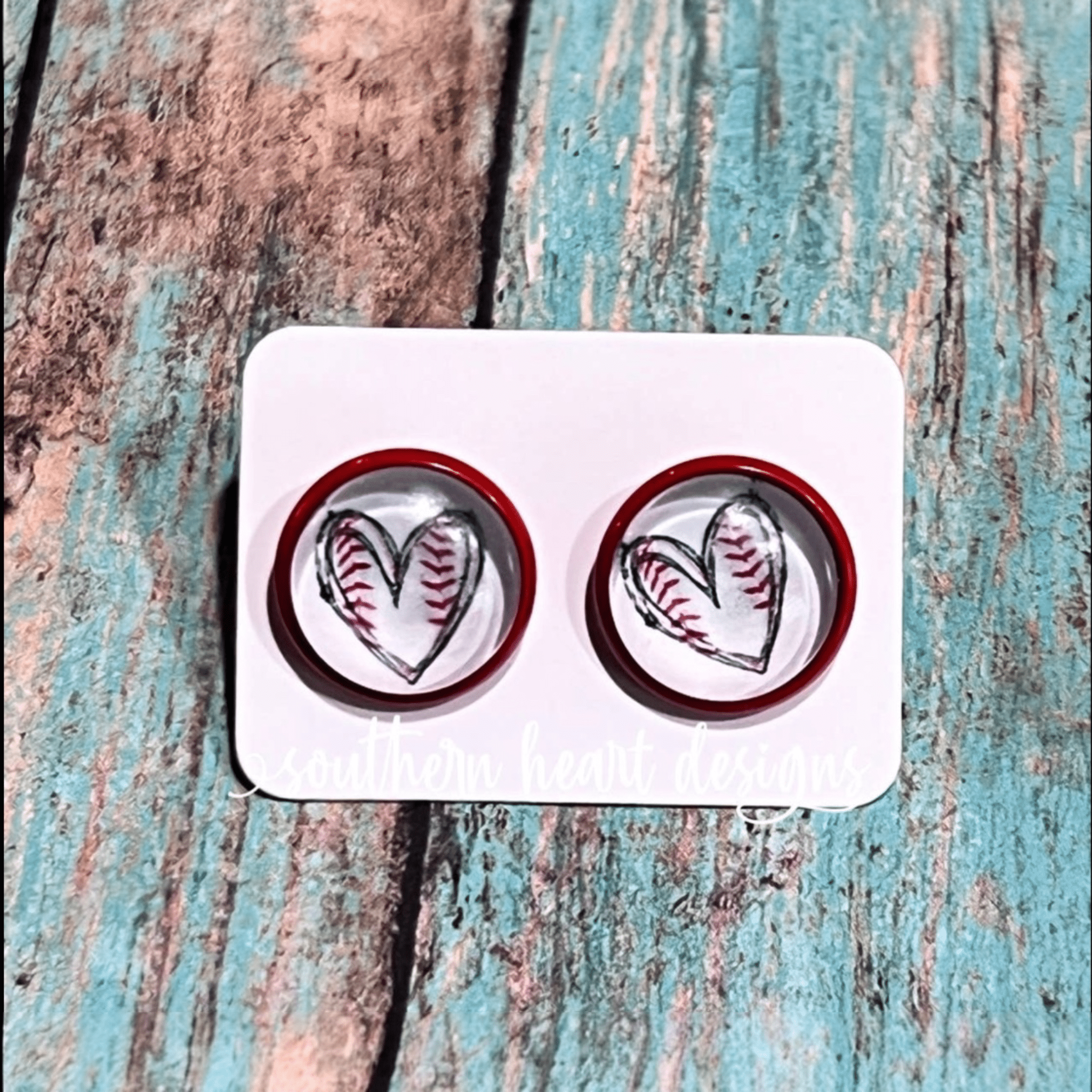 Heart-shaped inside a circle shape earrings with red borders on a white card against a textured wooden background