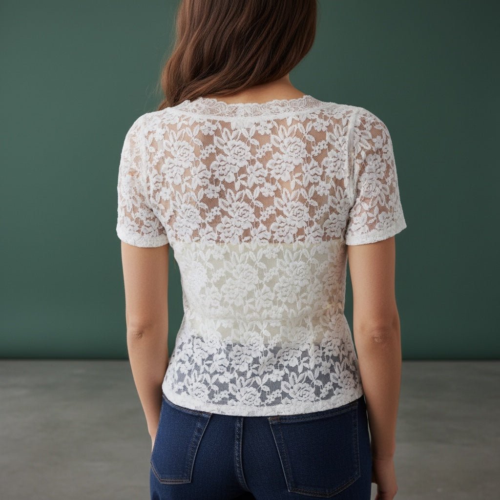 Person wearing a white lace top and blue jeans against a green background