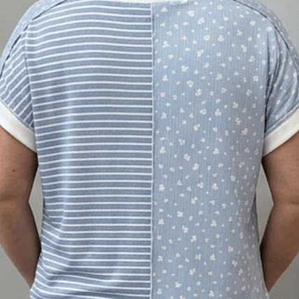 Person wearing a blue and white striped shirt with a patterned back, standing in front of a gray door.
