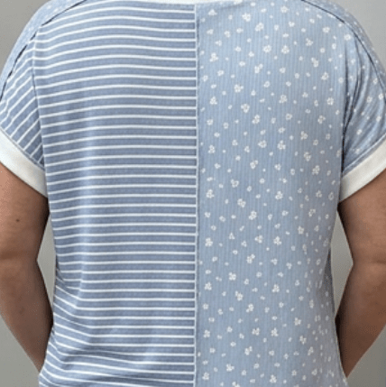 Person wearing a blue and white striped shirt with a patterned back, standing in front of a gray door.