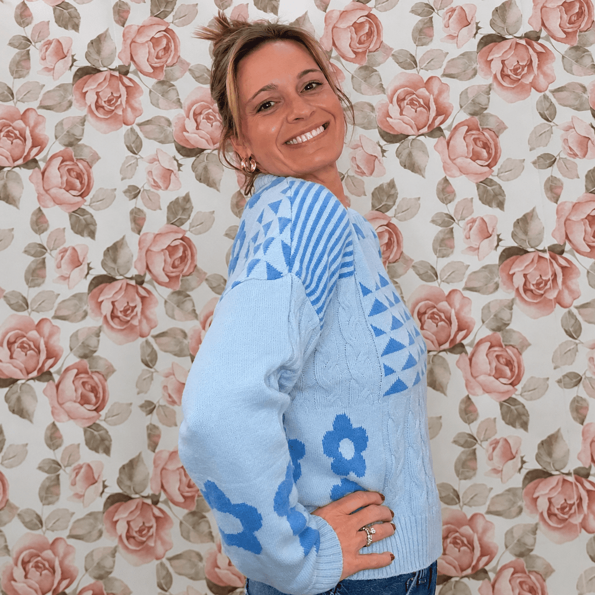 Side view of light blue floral knit sweater top showing cable knit detail, striped shoulder and blue daisy sleeve accents