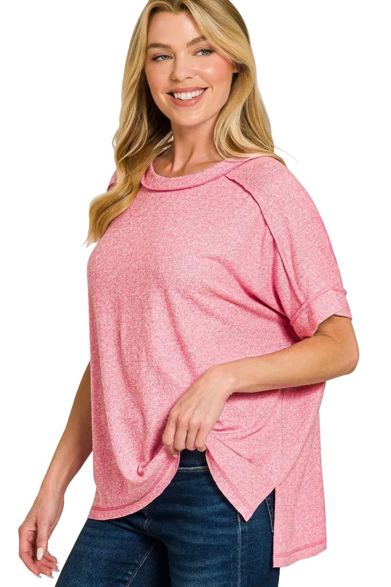 Woman wearing a candy pink melange tee with folded short sleeves, exposed seams and side slits, paired with dark jeans
