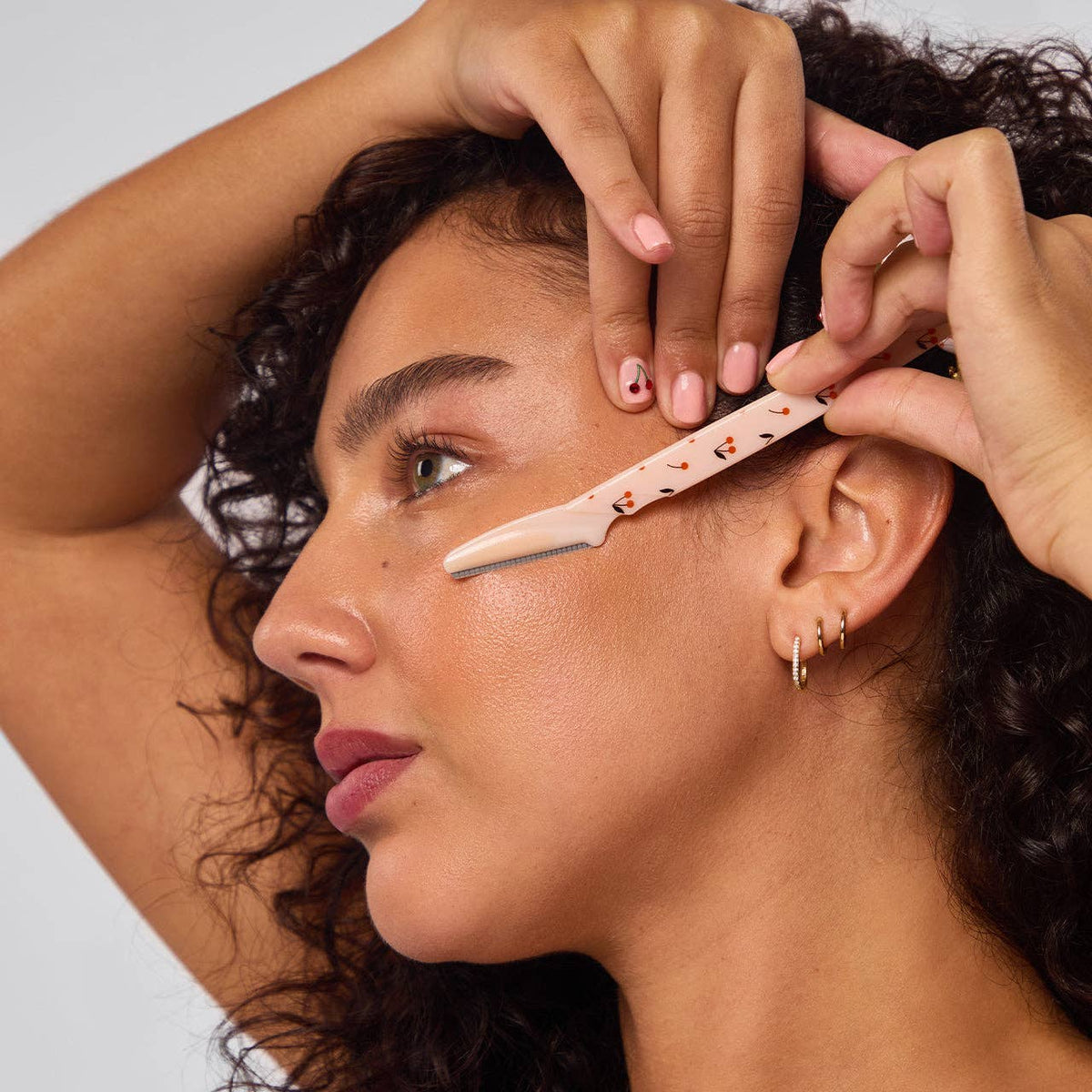 Woman using a cherry print KITSCH dermaplaner on her cheek to remove peach fuzz