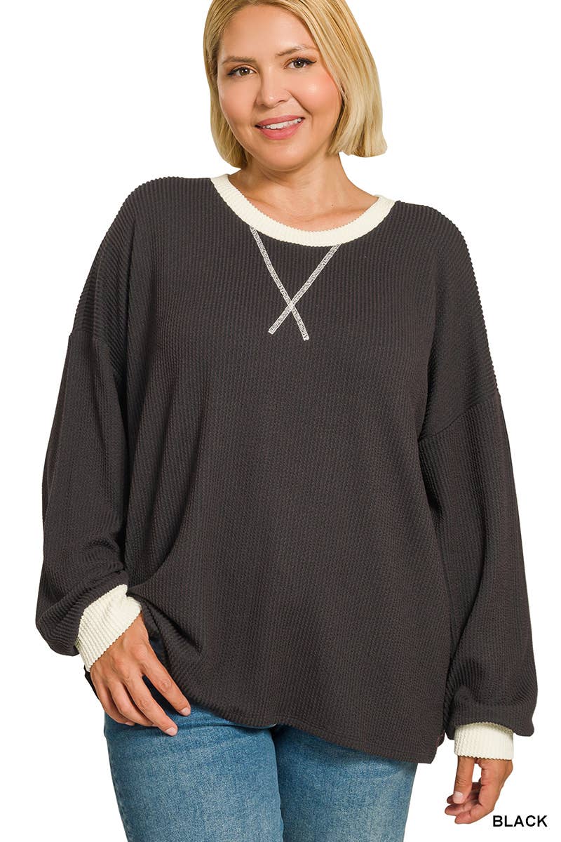 Woman wearing a plus size black raised rib pullover with cream contrast trim at the neck and cuffs and a V-stitch neckline, styled with light wash jeans
