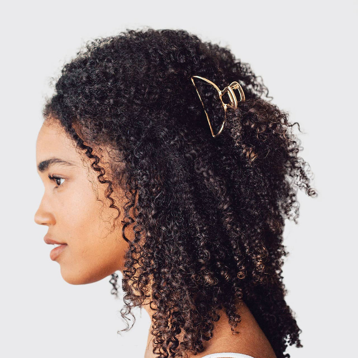 Woman with curly hair wearing a gold open shape claw clip in a half-up style