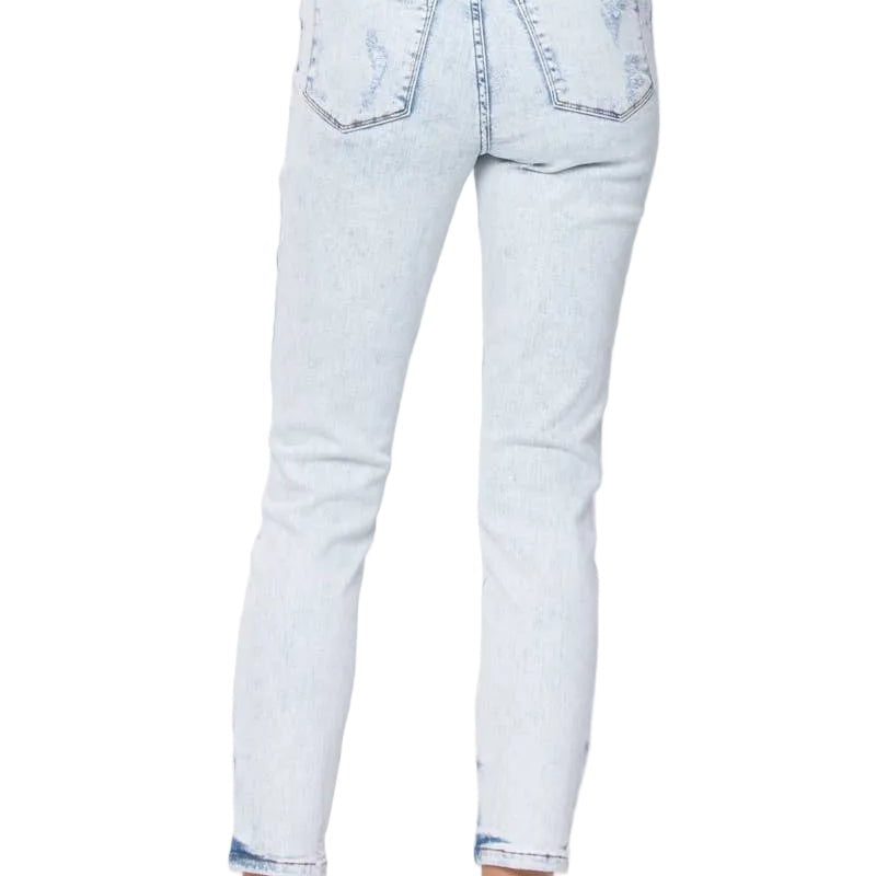 Rear view of a person wearing light-wash blue cropped denim jeans with rolled cuffs and flat brown slide sandals, against a plain light gray studio background.