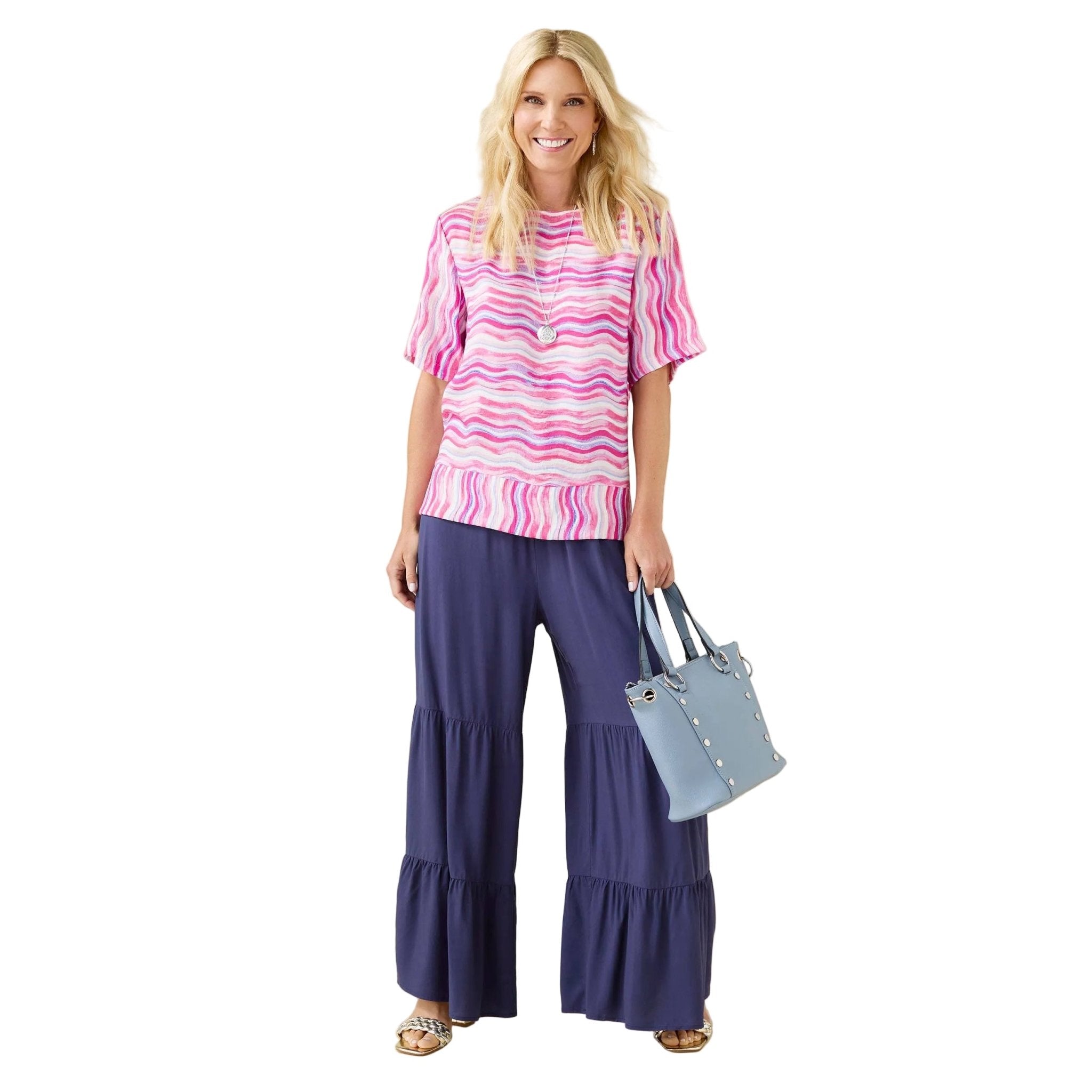 Woman wearing a pink and white striped top and navy blue pants, holding a light blue handbag on a beige background.