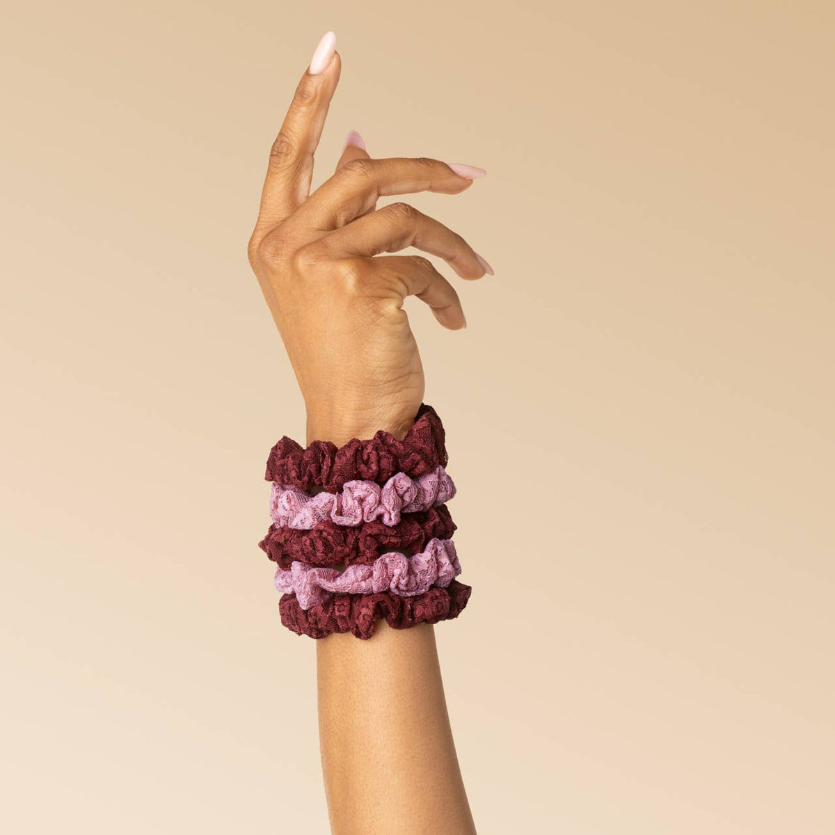 Burgundy and dusty pink lace scrunchies stacked on a wrist