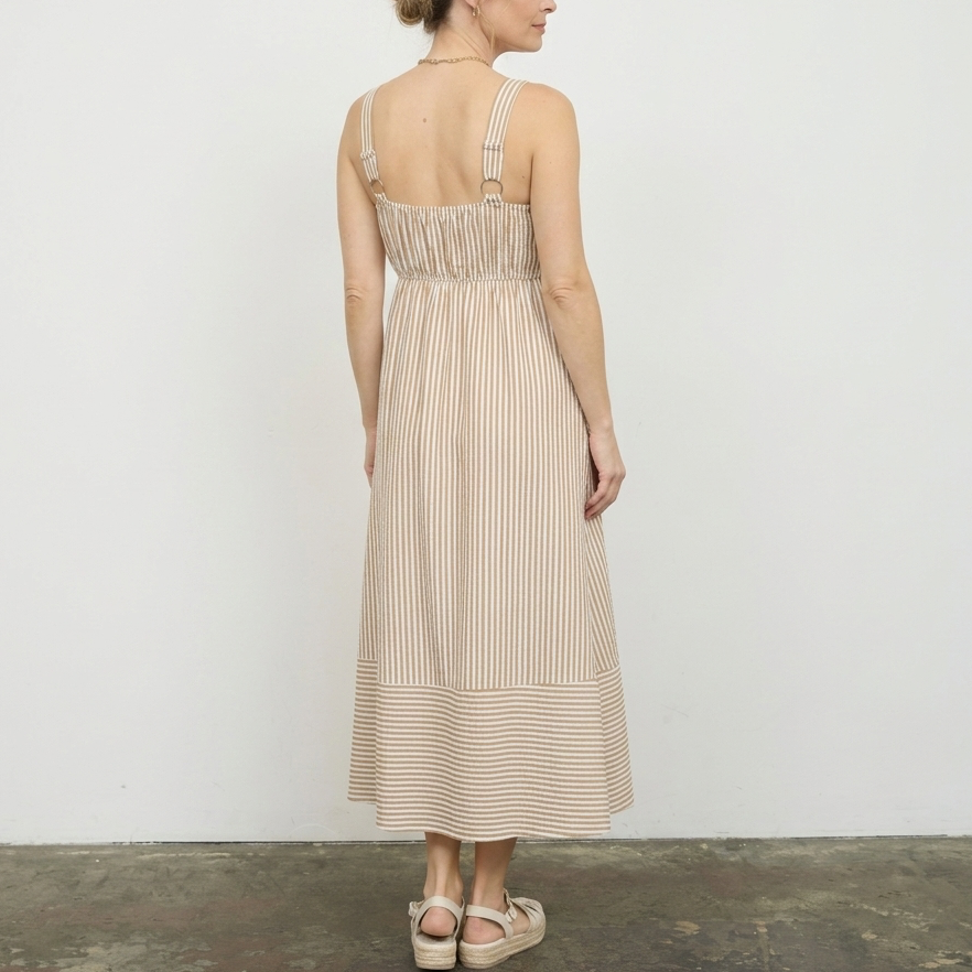 woman standing in a room wearing a beige stripped dress with sandals on