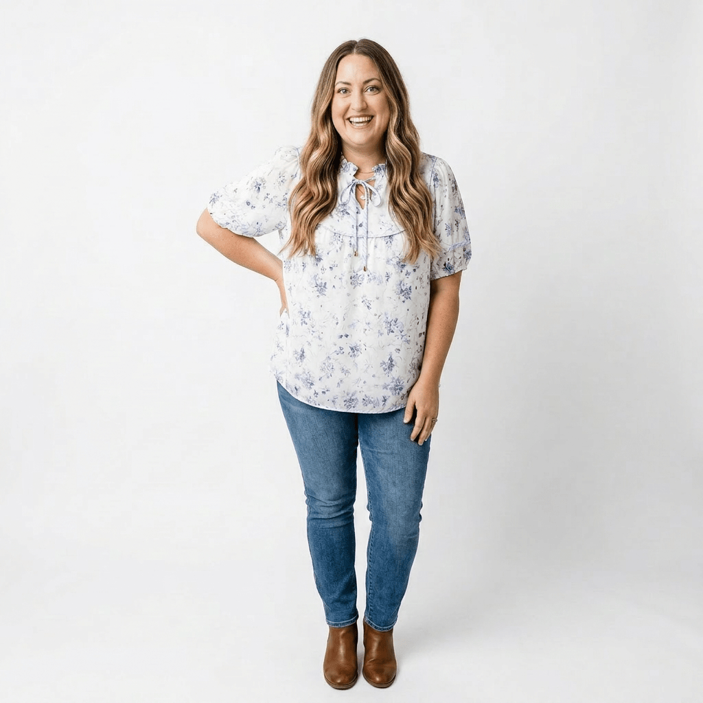 woman in purple floral top with white background. Wearing denim and brown boots.