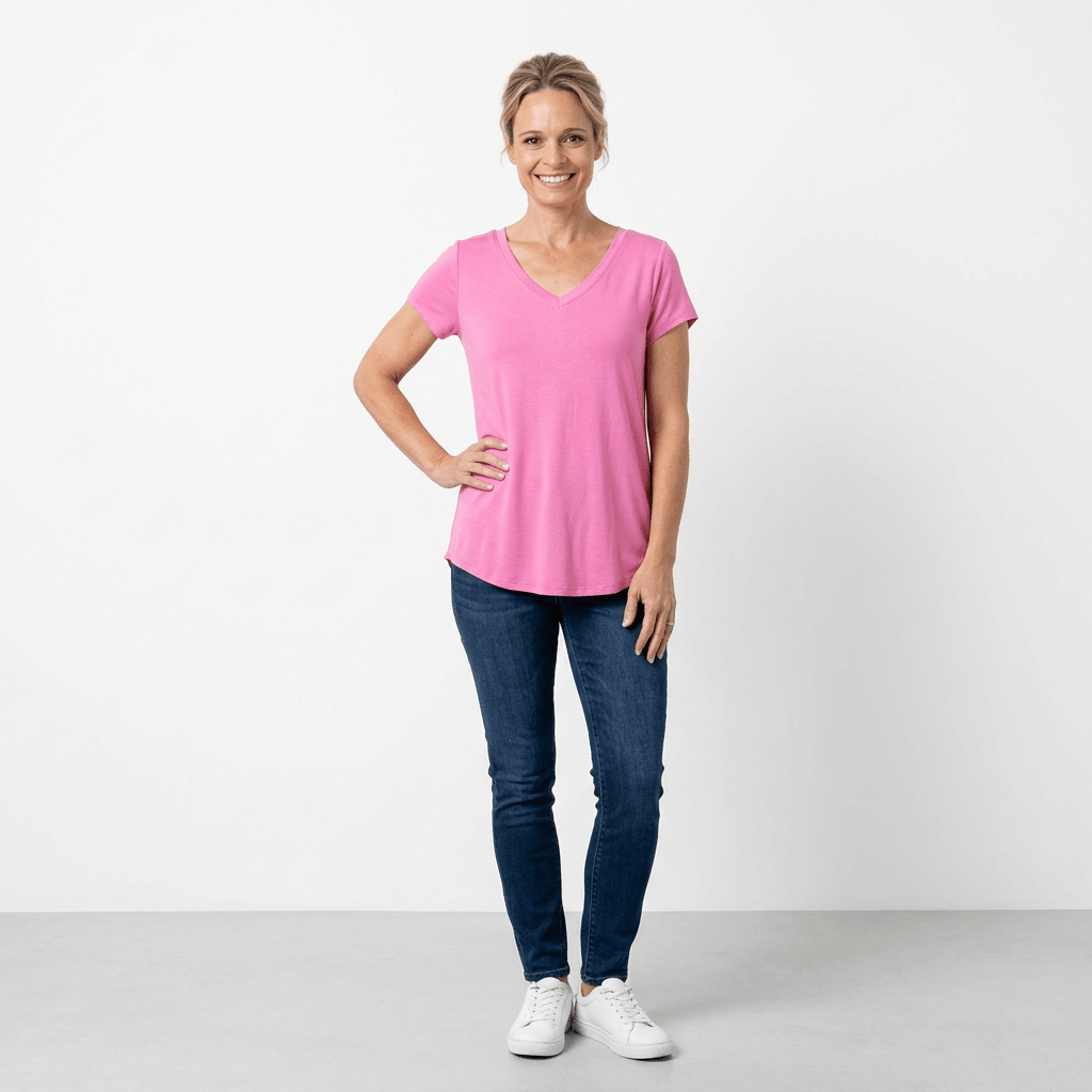 Woman wearing a pink t-shirt and blue jeans standing against a white background