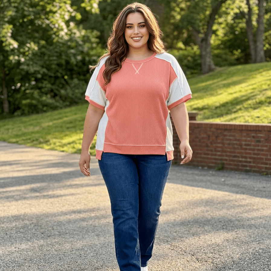 Woman walking outdoors wearing a coral and white top and blue jeans.