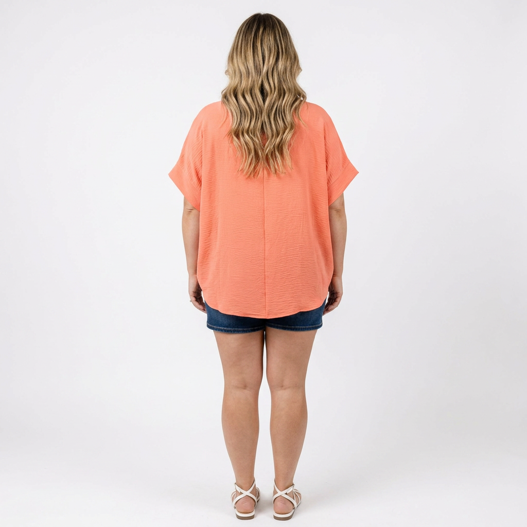woman wearing a coral top with denim shorts facing a white background