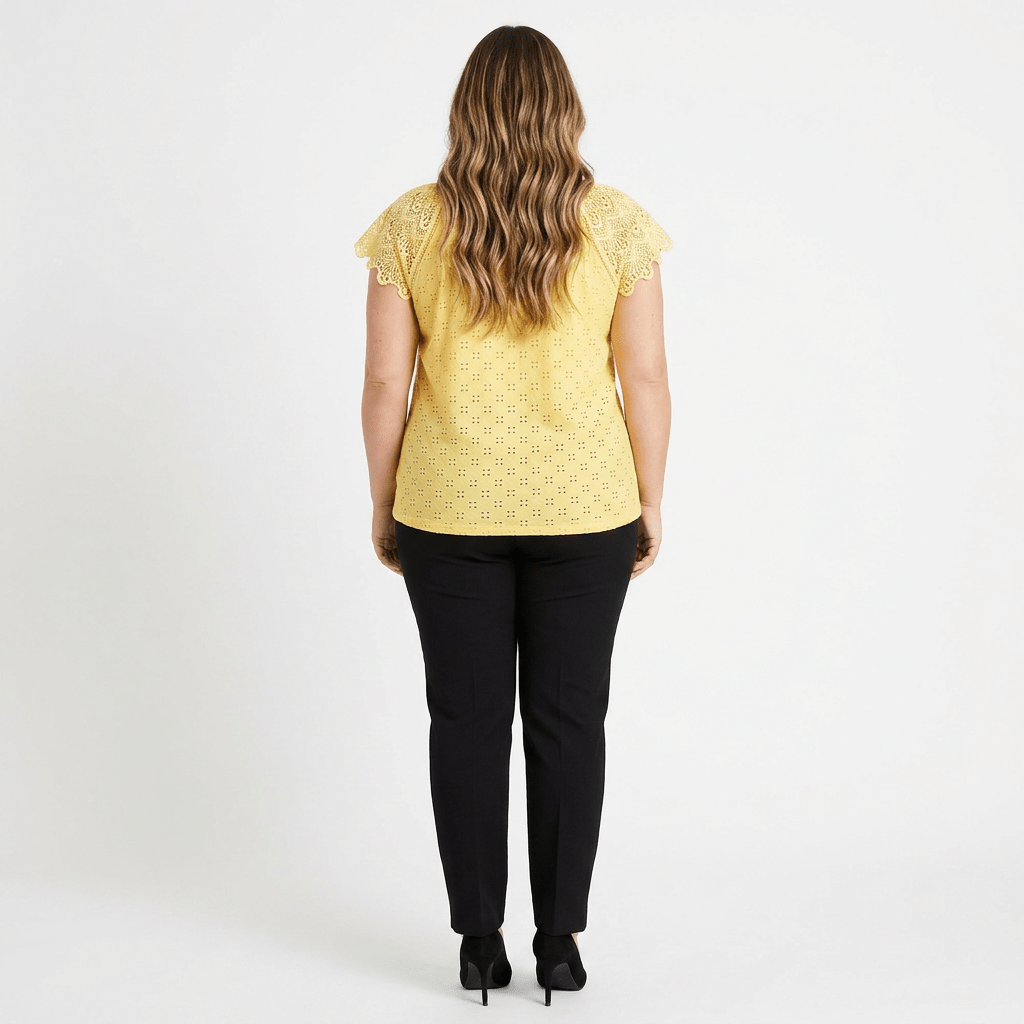 woman facing a white background wearing a yellow shirt with black pants