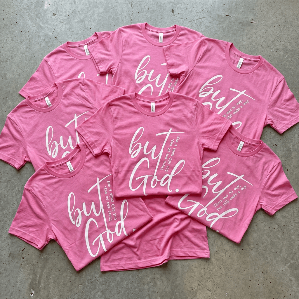 Pink t-shirts with 'but God' text on a gray surface