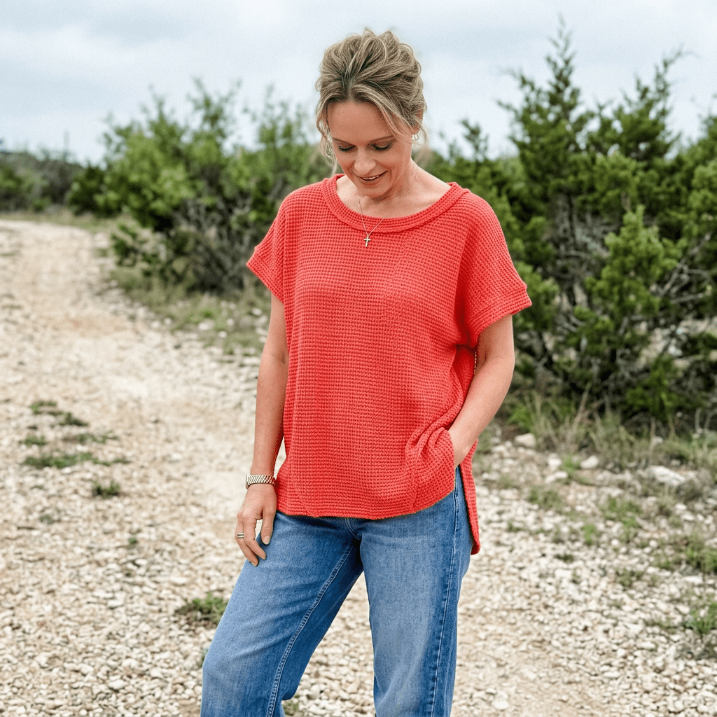 Women wearing red top with denim jeans standing on a gravel road.