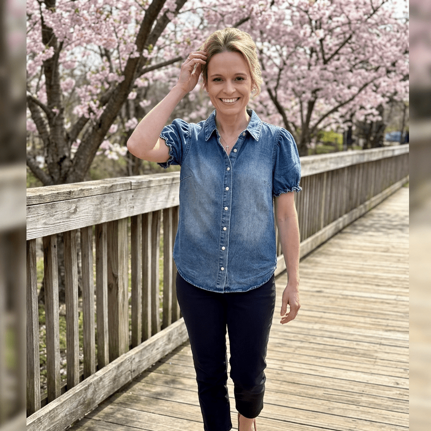 Woman in a denim shirt standing on a wooden bridge with cherry blossom trees in the background