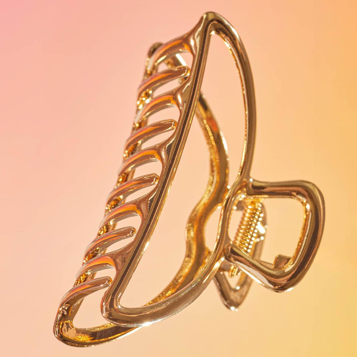 Gold open claw clip with a shiny finish on a peach background