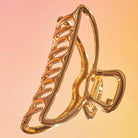 Gold open claw clip with a shiny finish on a peach background