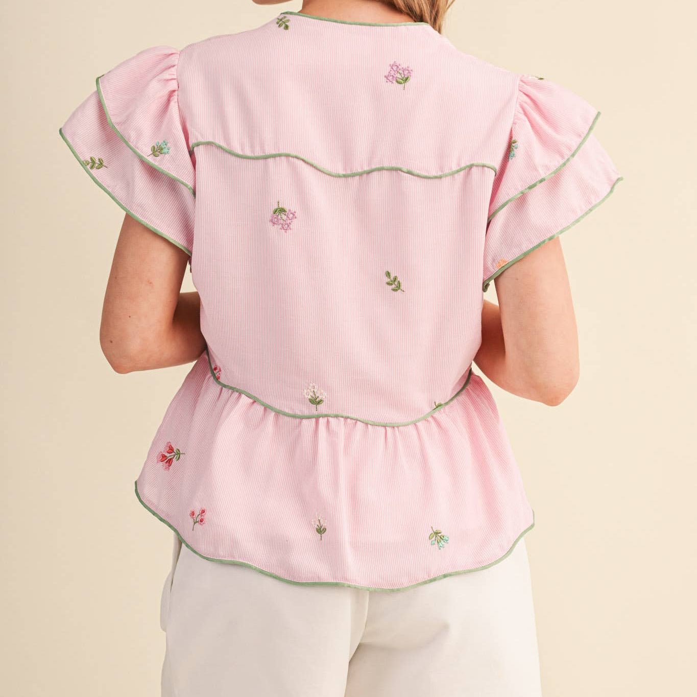 Woman wearing a pink embroidered top and white shorts on a beige background