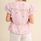 Woman wearing a pink embroidered top and white shorts on a beige background