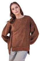 Woman wearing a chocolate brown oversized fleece top with a round neck, drop shoulders, ribbed hem and side slits, styled with light wash jeans