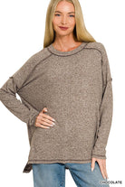 Woman wearing an oversized chocolate brown melange hacci knit top with exposed seams, long sleeves and a hi-low hem, paired with jeans