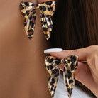 Leopard print bow earrings being worn and held up to an ear.