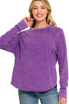 Woman wearing a violet mineral wash long sleeve top with a scoop neck, raglan sleeves and curved hem, paired with jeans