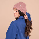 Woman in a blue coat wearing a blush pink satin-lined knit beanie, looking over her shoulder