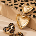 Heart-shaped earrings with gold and leopard print design on a patterned surface