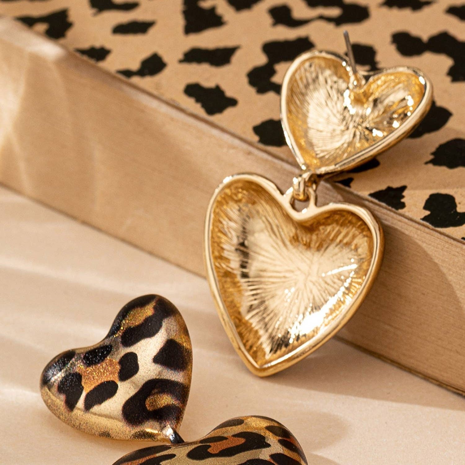 Heart-shaped earrings with gold and leopard print design on a patterned surface